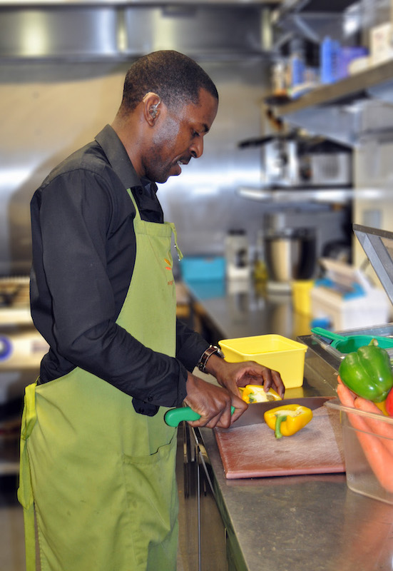 Wycliffe is cutting vegetables in the cafe's kitchen.